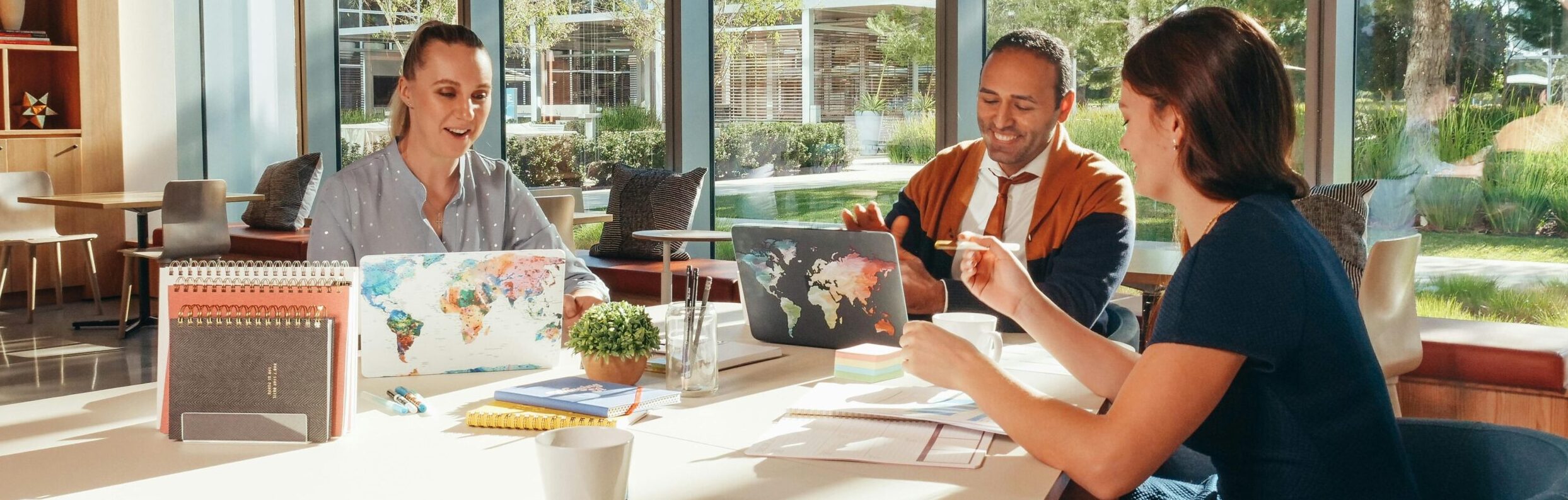 Three colleagues brainstorming with laptops in a well-lit office.